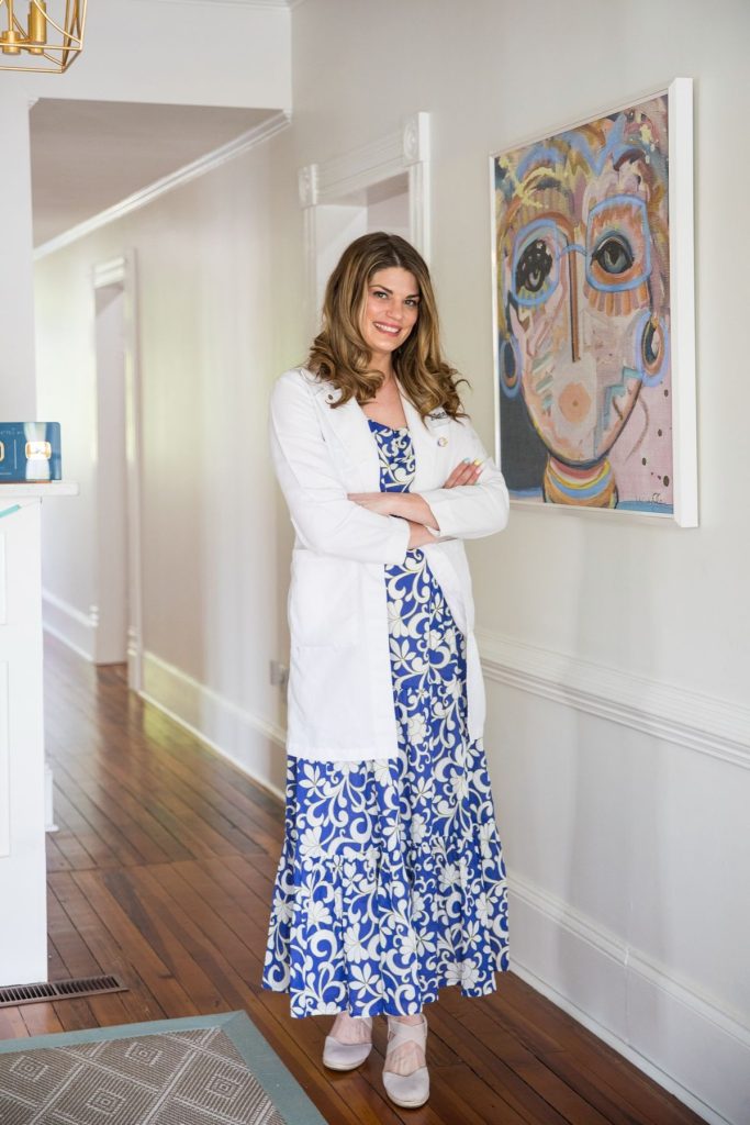 Dr. Melanie Denton in her white coat standing in a hallway at Salisbury Eyecare & Eyewear beside colorful artwork
